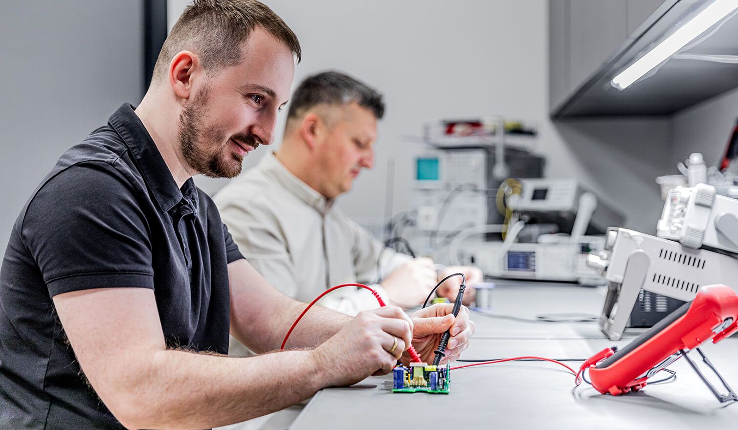 Dva technici v elektronickém laboratoři, kteří provádějí přesné montážní úkony za vhodných světelných podmínek