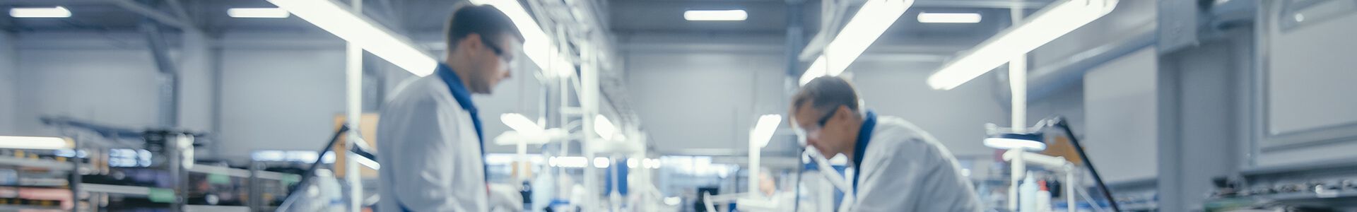 Dva muži v laboratorních pláštích pracují v moderní laboratoři na výrobě elektroniky