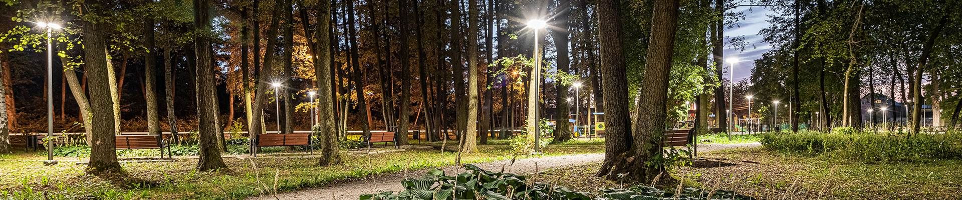Oświetlone alejki i ławki w parku po zmroku – oprawy parkowe LED Lena Lighting w Parku Łochów